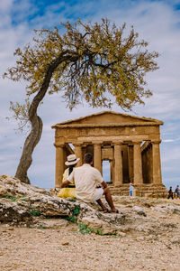 Rear view of man sitting against built structure