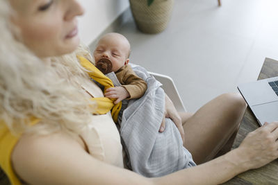 Baby boy sleeping in arms of woman working from home