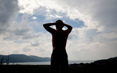 Silhouette woman with arms raised standing on mountain against sky