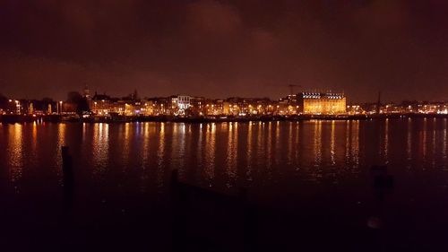 Illuminated cityscape by river against sky at night