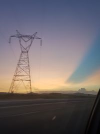 Silhouette electricity pylon by road against sky during sunset