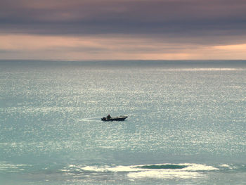 Boat on sea against cloudy sky during sunset