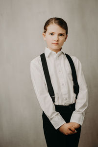 Portrait of girl wearing suspenders and shirt against white background