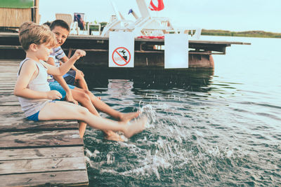 Playful kids having fun while sitting on a pier and splashing water.