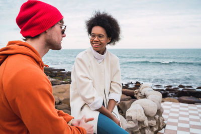 Young couple sitting on sea shore against sky