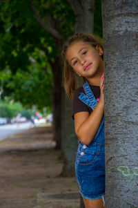Portrait of happy girl leaning on tree trunk