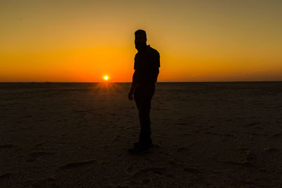 Silhouette man standing at great rann of kutch against sky during sunset