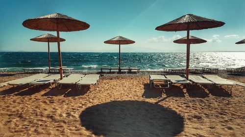 Parasol by deck chair on sand at beach against sky