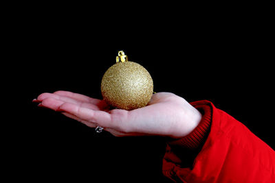 Close-up of hand holding golden bauble against black background