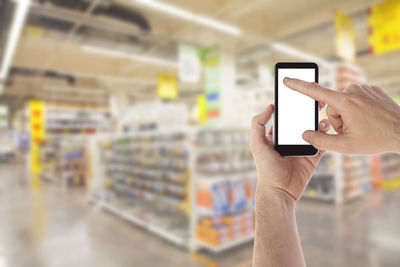 Cropped hands holding mobile phone at supermarket