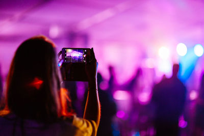 Rear view of woman photographing in popular music concert at nightclub