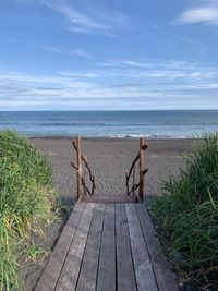 Walkway leading towards sea against sky