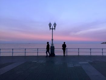 Silhouette people on promenade against sea during sunset