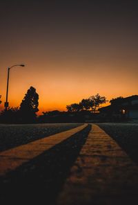 Road by silhouette trees against clear sky during sunset