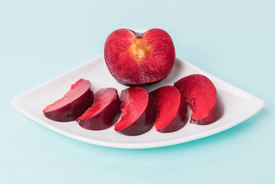 On a white saucer, a large plum, cut in half, with slices next to it.