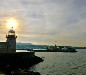 Lighthouse by sea against sky during sunset