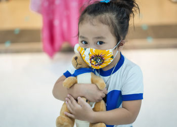 Portrait of cute girl wearing mask playing with teddy bear