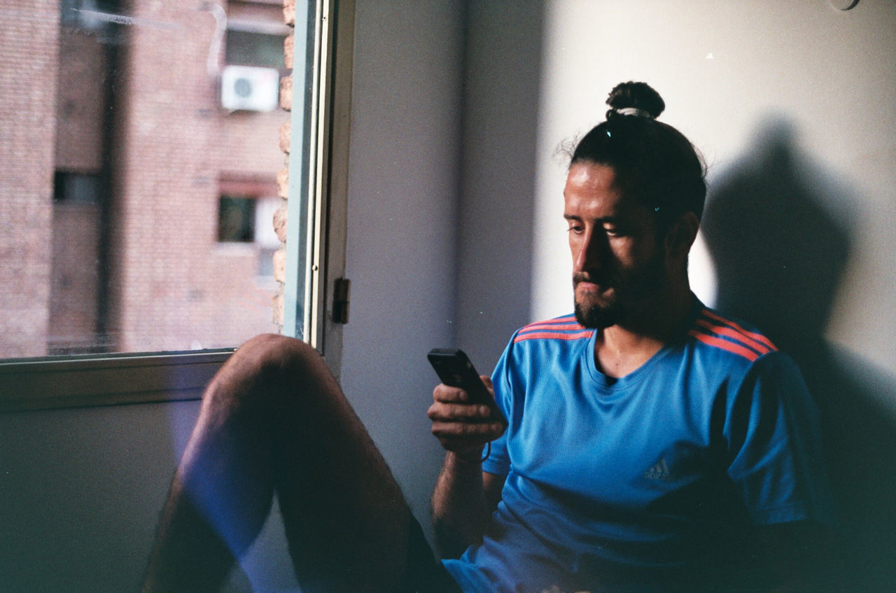 YOUNG MAN USING PHONE WHILE SITTING IN LAPTOP