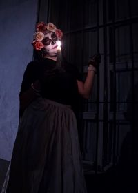 Midsection of woman wearing mask against dark wall at night