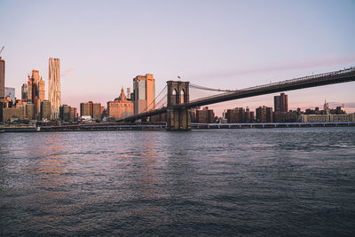 View of suspension bridge over river with buildings in background