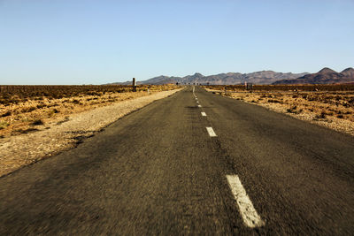 Road leading towards mountains against clear sky