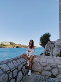 Portrait of young woman standing by sea against clear sky