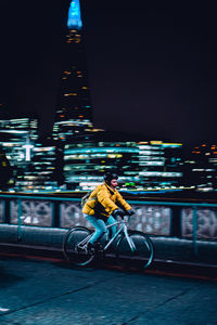 Man riding bicycle on illuminated street at night