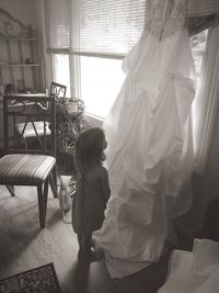 Rear view of little girl looking at dress hanging on window