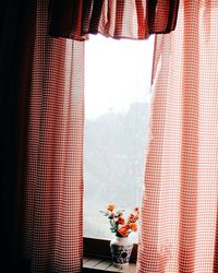 Orange flower vase amidst curtain on window