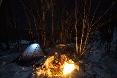 Man sitting by bonfire in forest at night