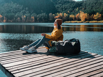 Woman sitting by lake against trees