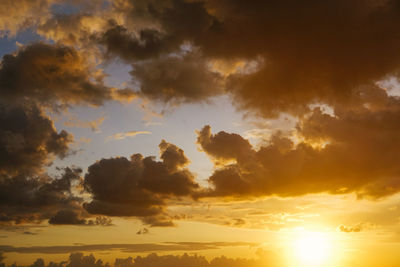 Low angle view of sunlight streaming through clouds during sunset