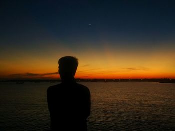 Rear view of silhouette man standing at beach during sunset