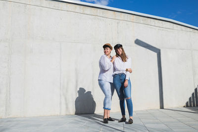 Full length of a smiling young woman standing against wall