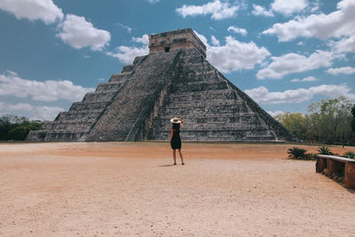 Rear view of woman walking on historical building against cloudy sky