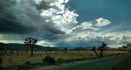 Road passing through field against cloudy sky