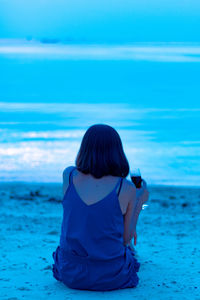 Rear view of woman having drink while sitting at beach