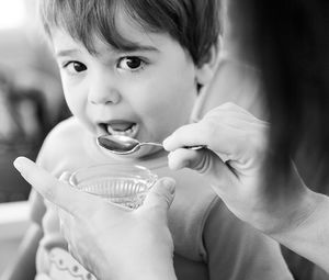 Cropped hands of mother feeding son sitting at home