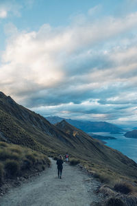 Rear view of woman walking on road by mountain against sky