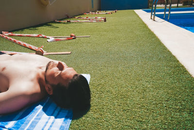 Shirtless man lying on grass by swimming pool