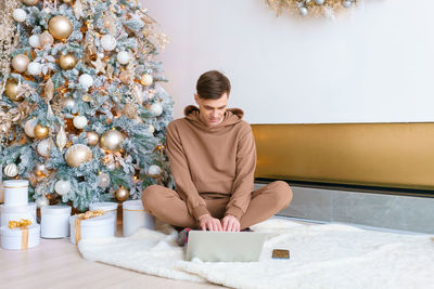 A man sitting on floor near christmas tree orders online goods on black friday