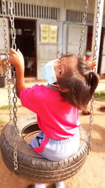 Portrait of girl in mask sitting on swing