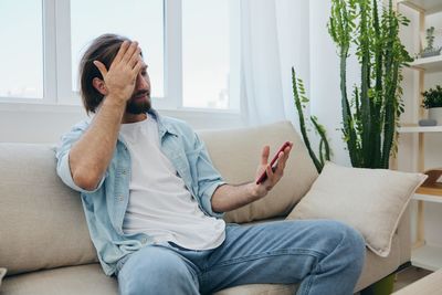 Young woman using phone while sitting on sofa at home