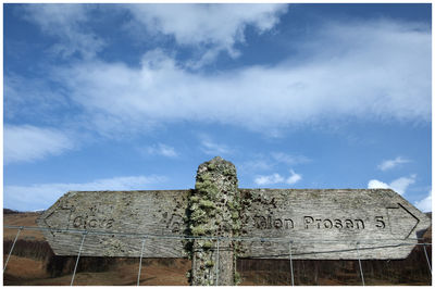 Low angle view of sign on wood against sky