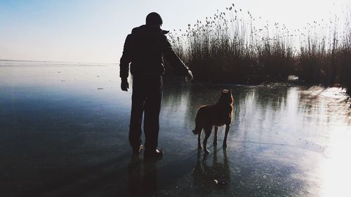 Silhouette man with dog on frozen lake