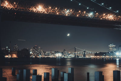 Illuminated city by river against sky at night