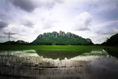 Scenic view of pond by mountain against cloudy sky