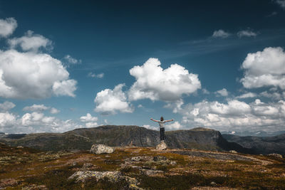 Woman with arms outstretched while standing on rock against sky