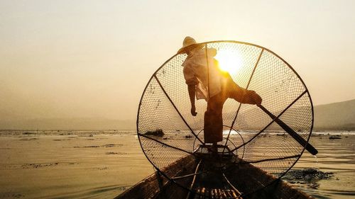 Man fishing in inle lake against sky during sunset