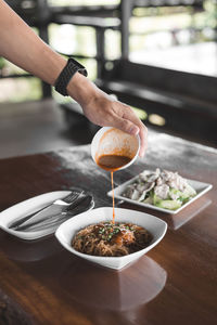 Cropped hand of woman pouring sauce in noodles at home